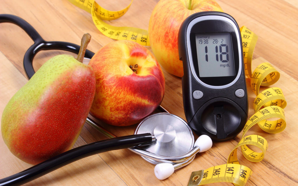 a glucose monitor, a stethoscope and some fruit on a table