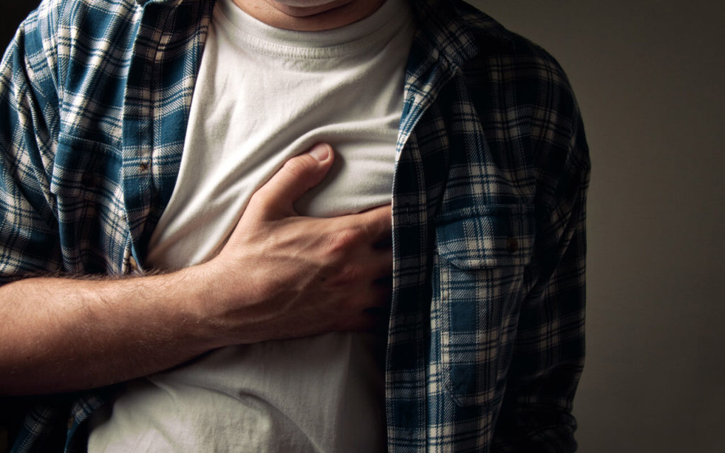 man with unbuttoned shirt and white t-shirt holding his heart